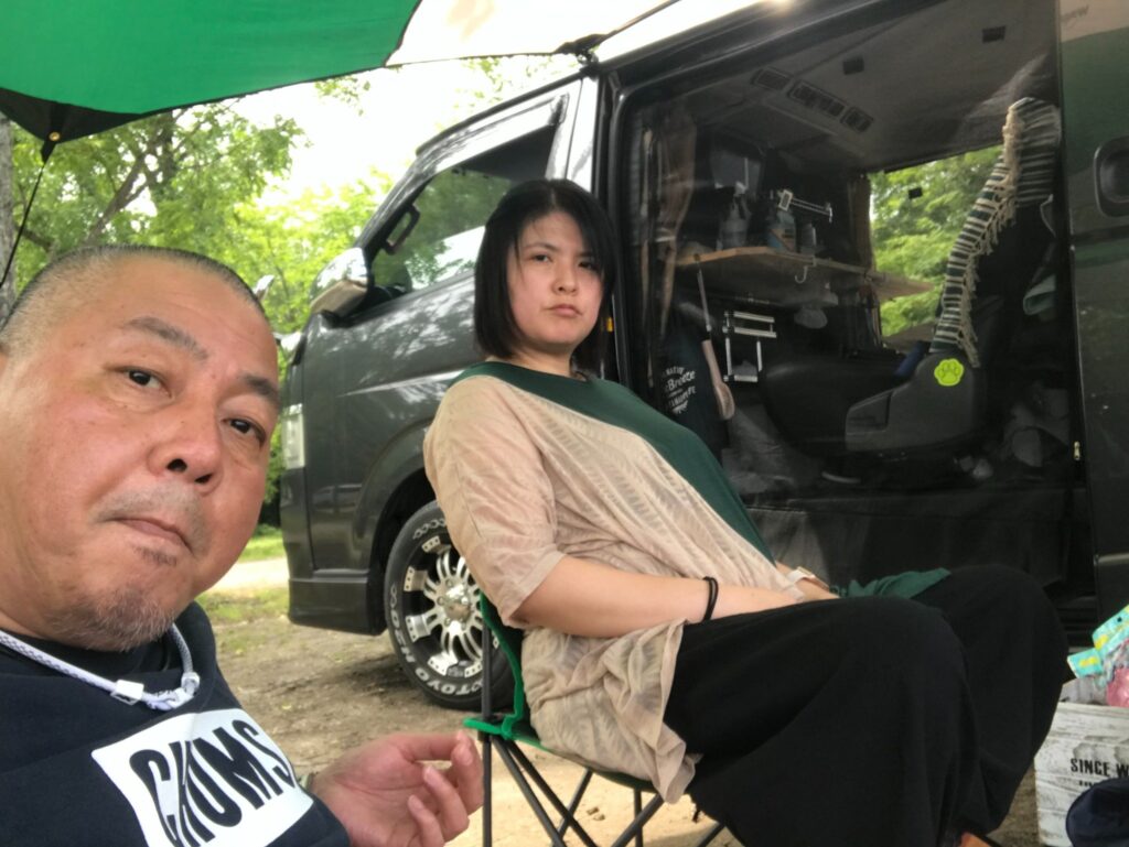 タープの下で椅子に座り、車中泊を楽しむ2人