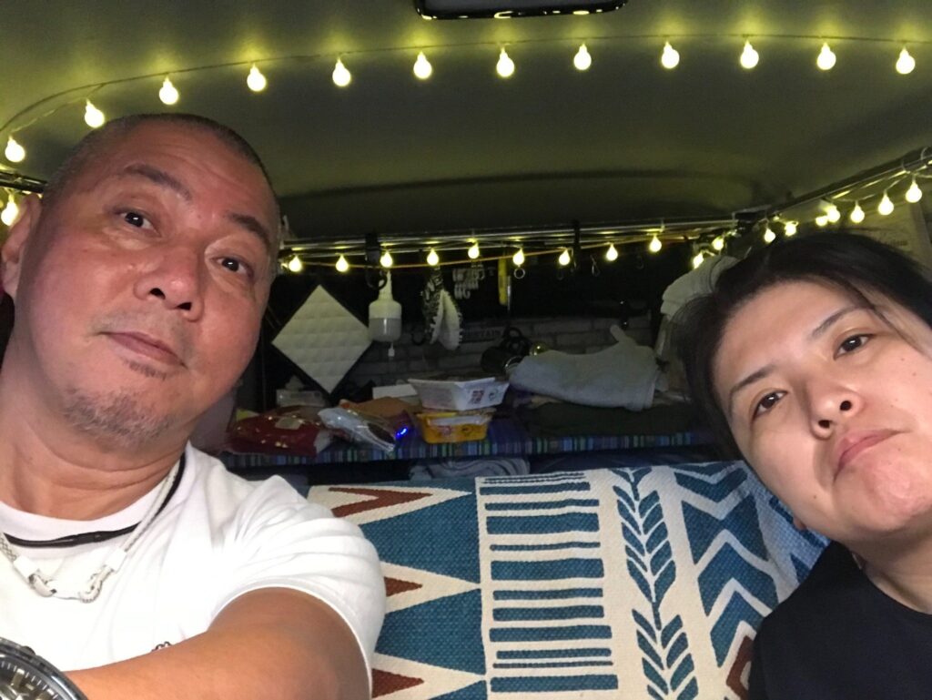 ハイエースの車内でくつろぐ夫婦の様子（夜・ライト付き）