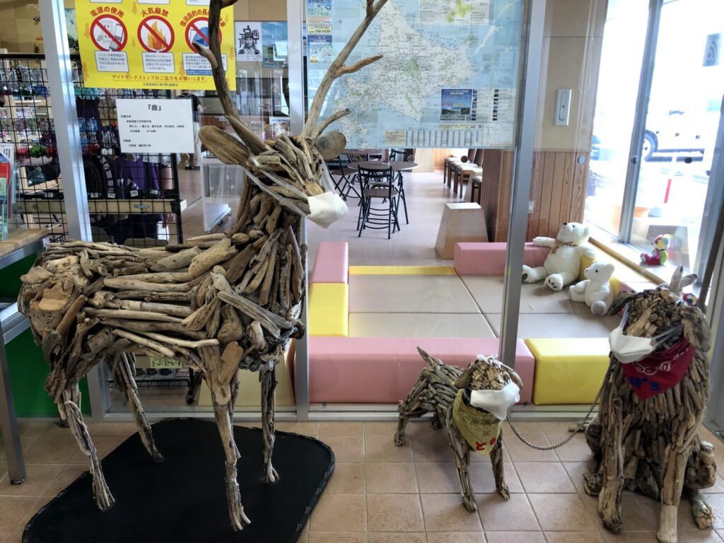 道の駅オスコイ！かもえないに展示されているマスク姿の流木アート作品（鹿と犬）