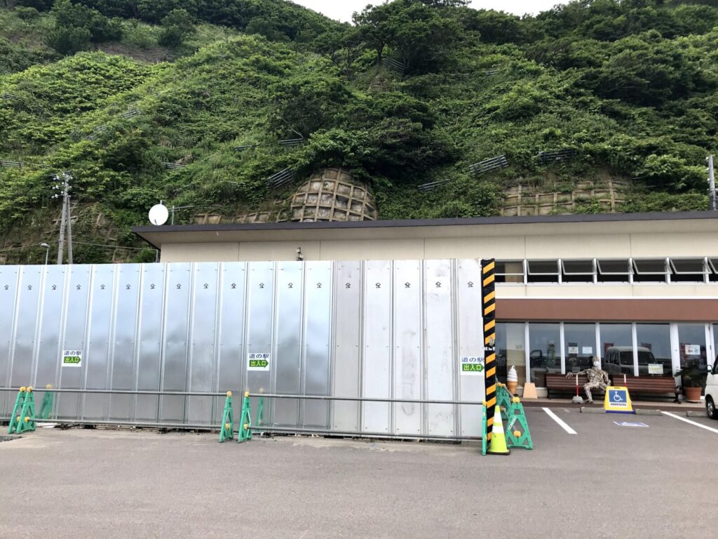 道の駅オスコイ！かもえないの外観と、背後に迫る緑の山肌が見える風景
