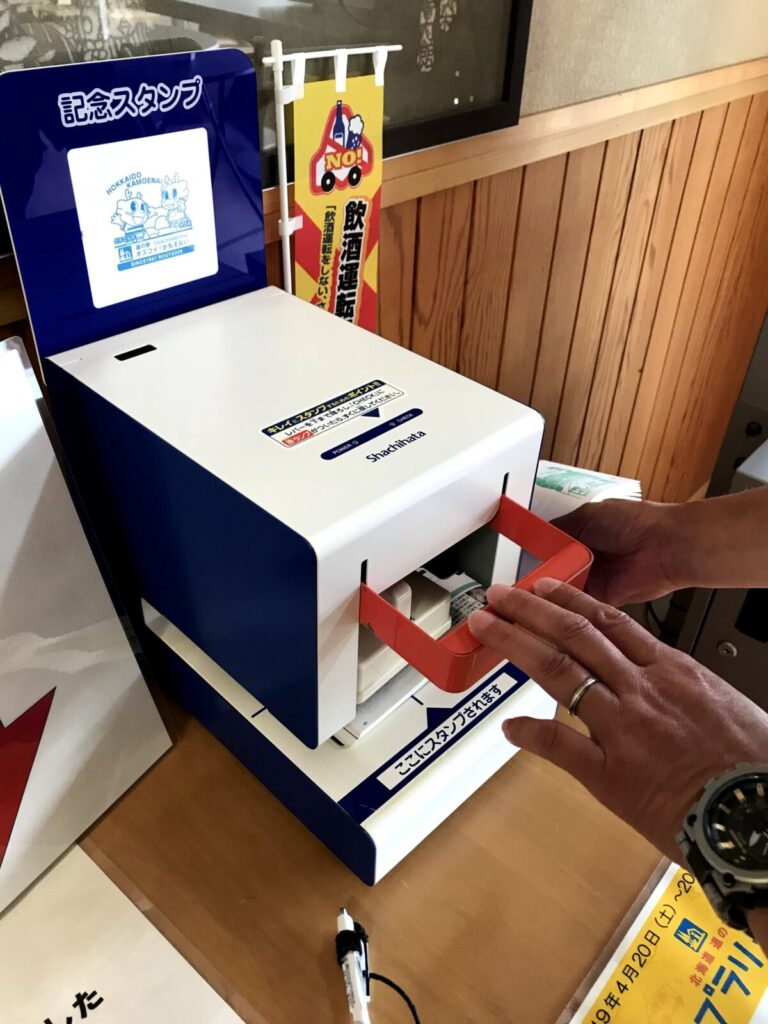 道の駅オスコイ！かもえないの自動スタンプ機にスタンプ帳をセットして押している様子