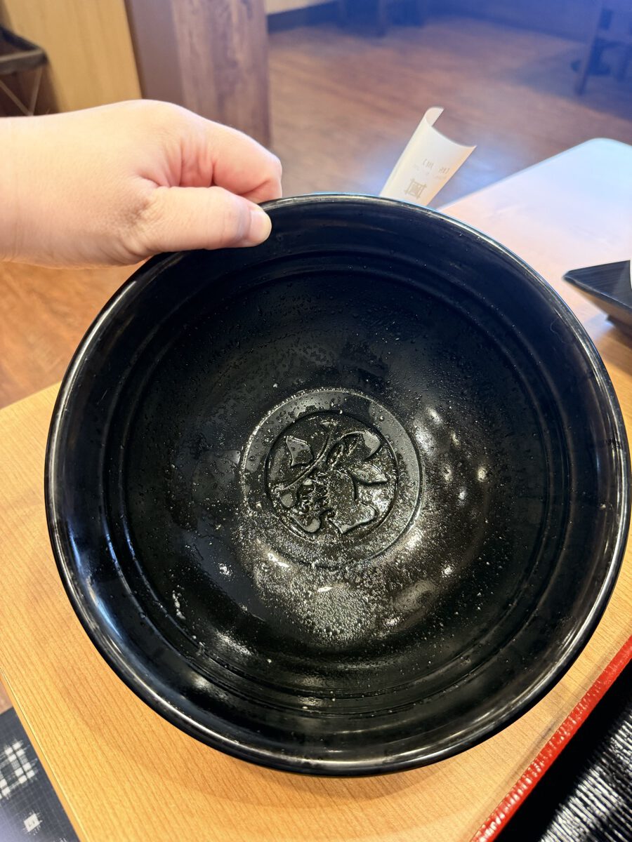 資さんうどんの黒い器の底に刻印された「資」のロゴ